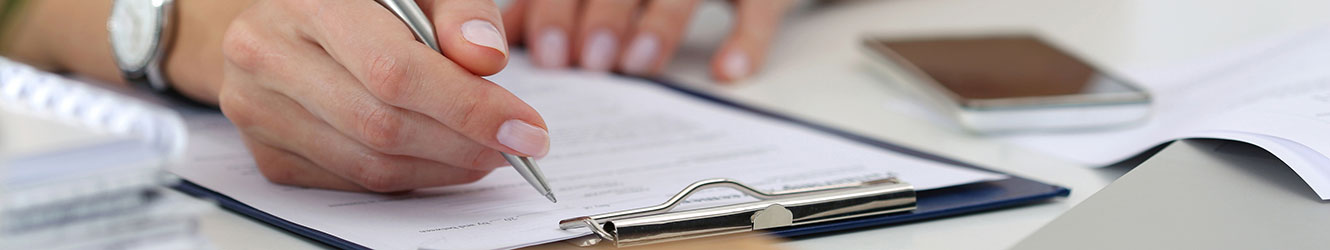 Woman holding pen with paperwork on clipboard.