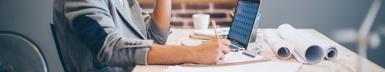 Man sitting at desk writing, with laptop.