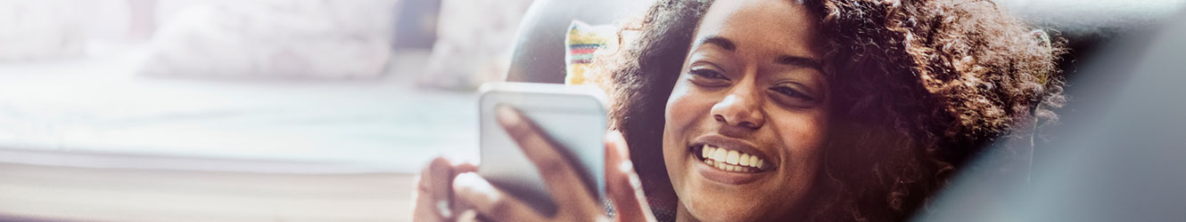 Woman laying on couch holding mobile and smiling.